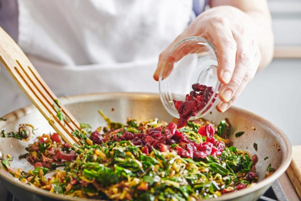 Woman adding cranberries to a skilled of swiss chard and leek.