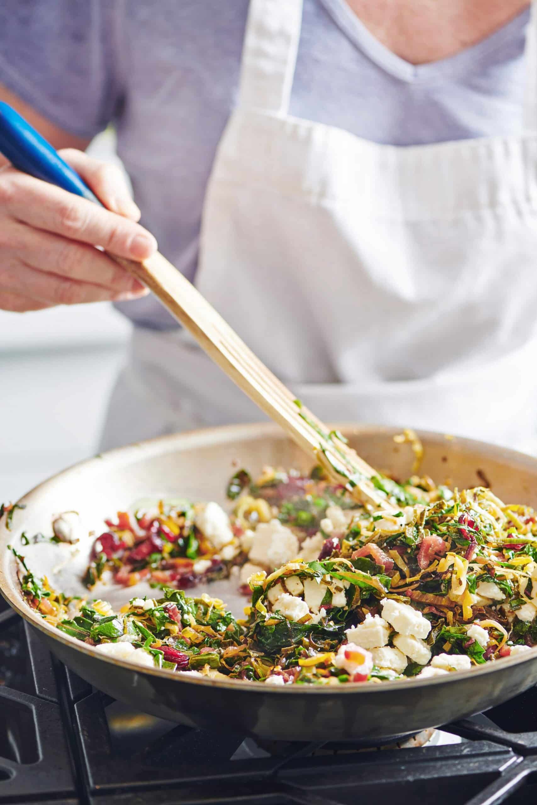Woman stirring a skillet of Swiss Chard, Leek and Feta.