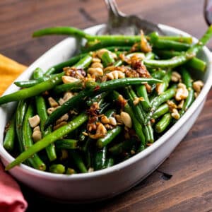 Thai-style green beans in white serving dish on wood table.