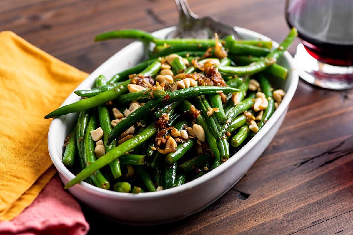 Thai-style green beans in white serving dish on wood table.
