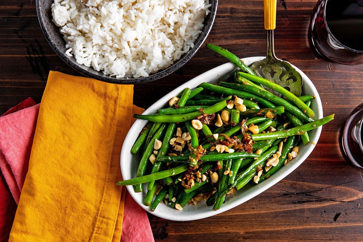 Decorative spatula in a dish of Thai Green Beans on table with bowl of rice.