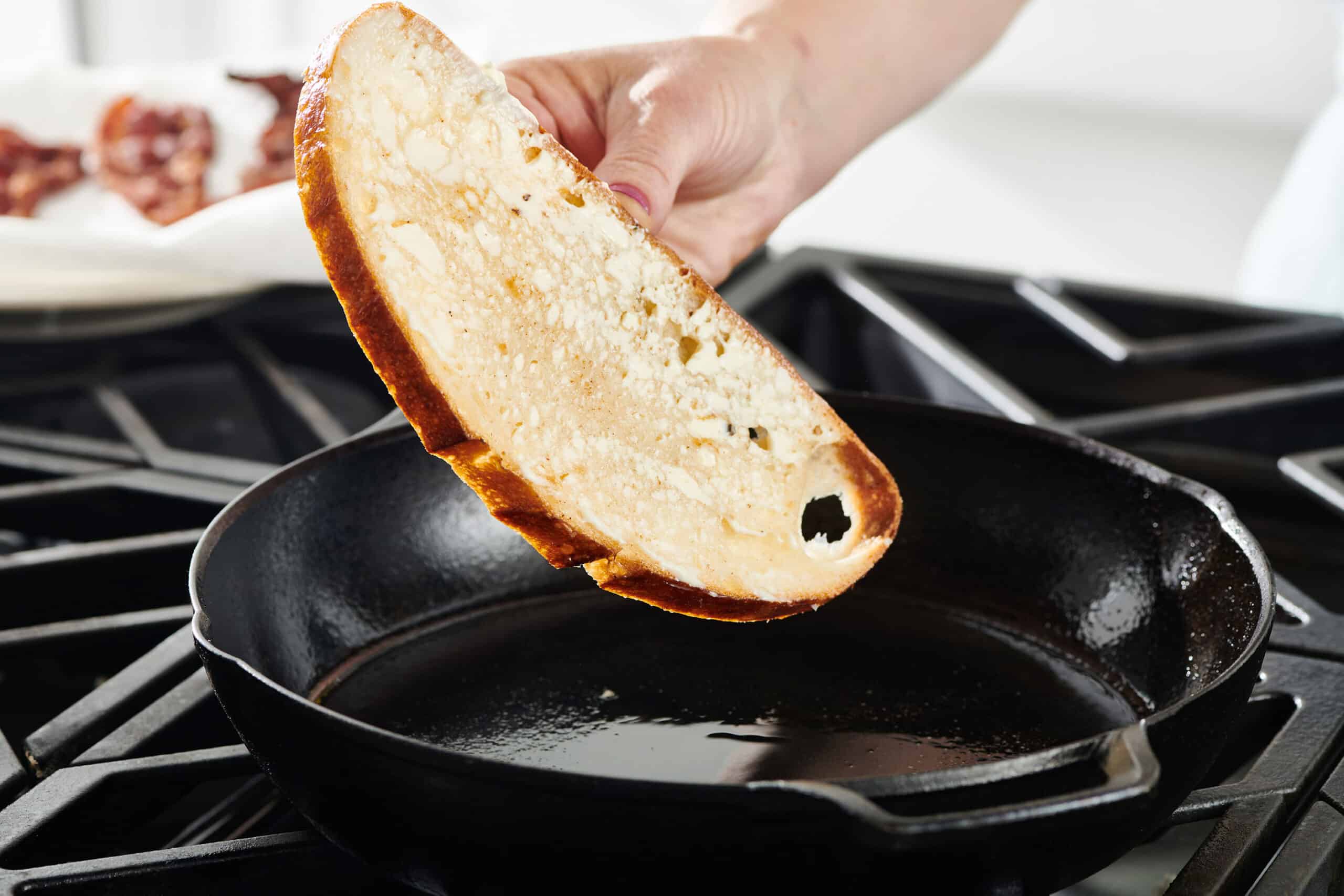 A woman's hand placing a slice of bread spread with mayonnaise in a skillet on the stove