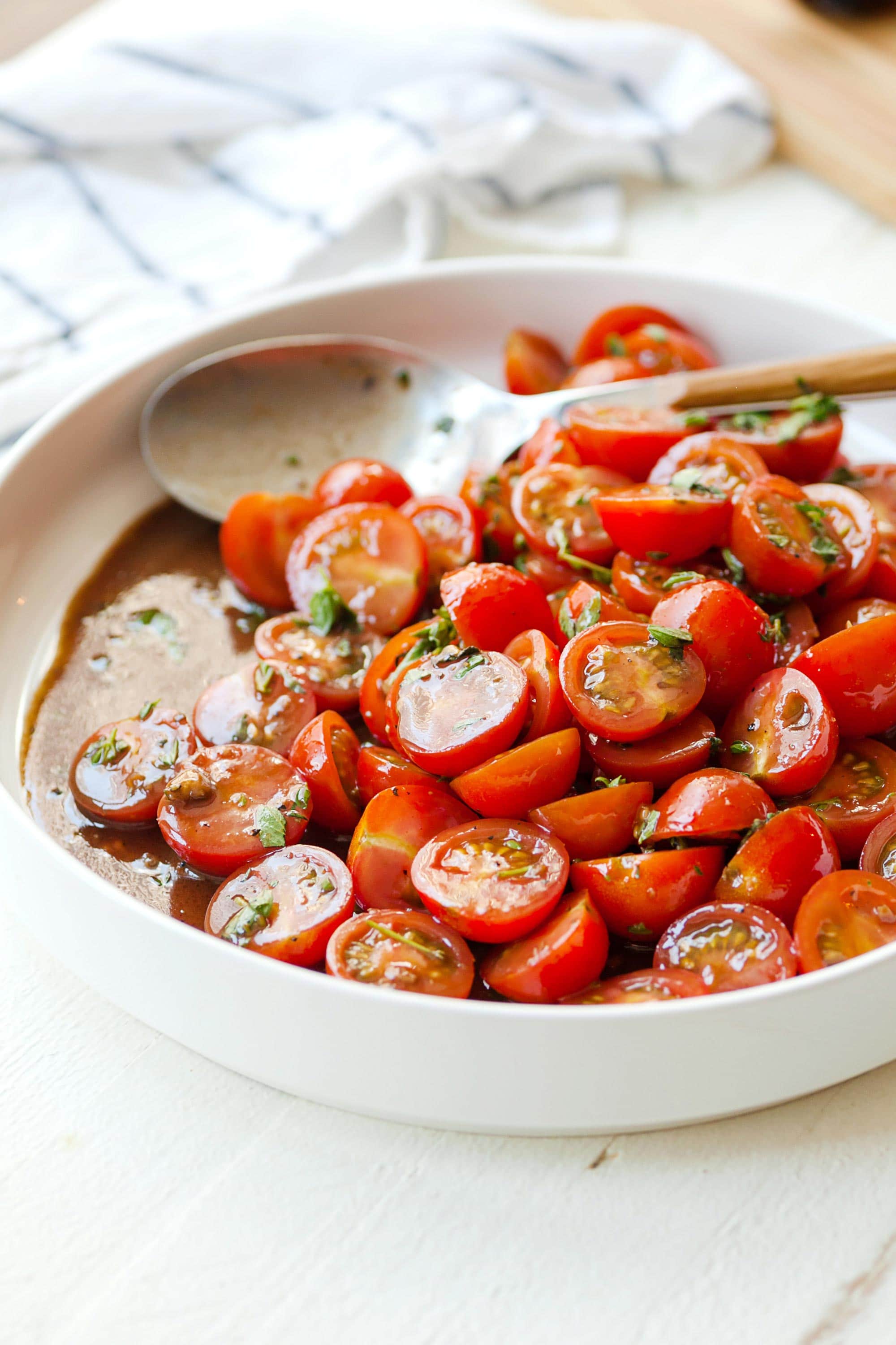 Cherry Tomato Salad in white bowl with serving spoon and towel.