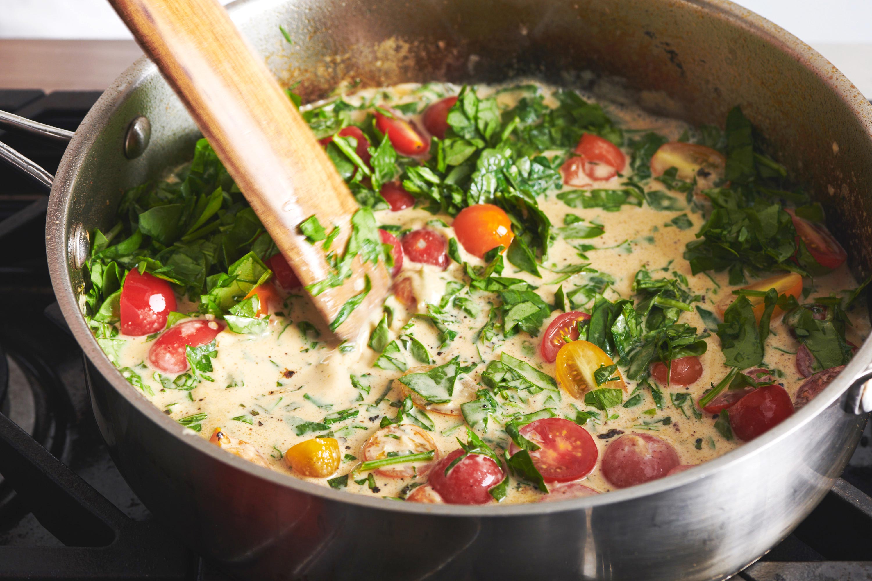 Stirring pa sauce with tomatoes for Creamy Tuscan Chicken.