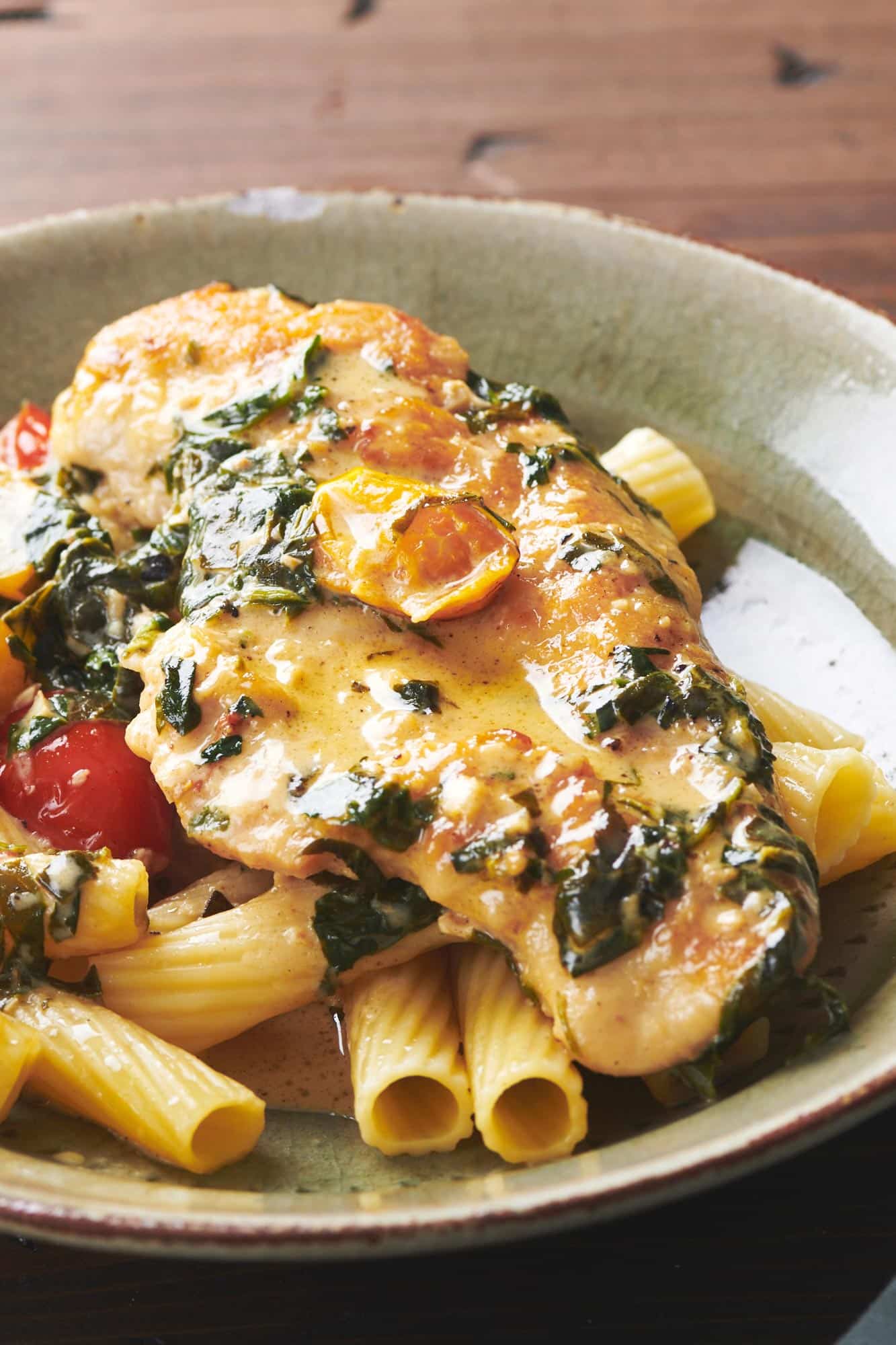 Creamy Tuscan Chicken over noodles on a plate.