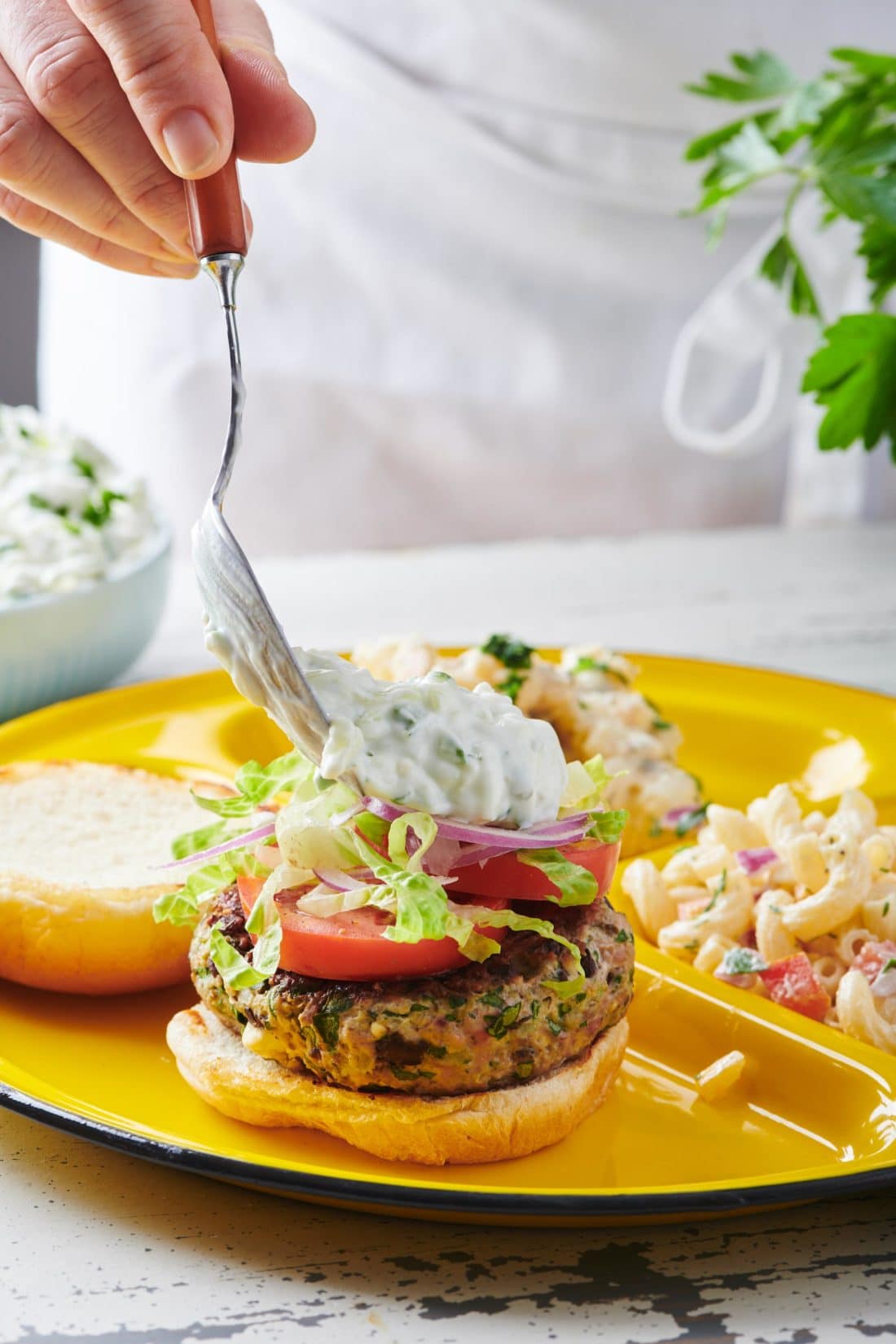 Spoon topping a Greek Turkey Burger with tzatziki.