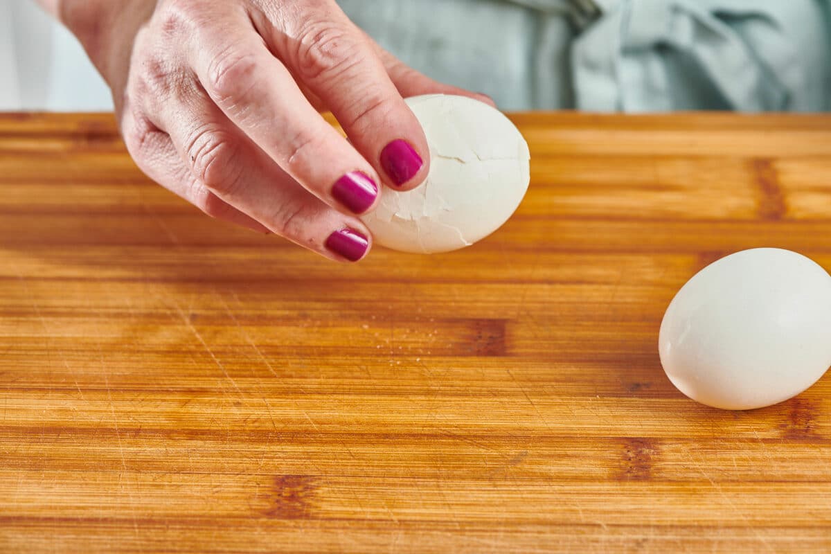 Woman holding a hard boiled egg with a cracked shell.