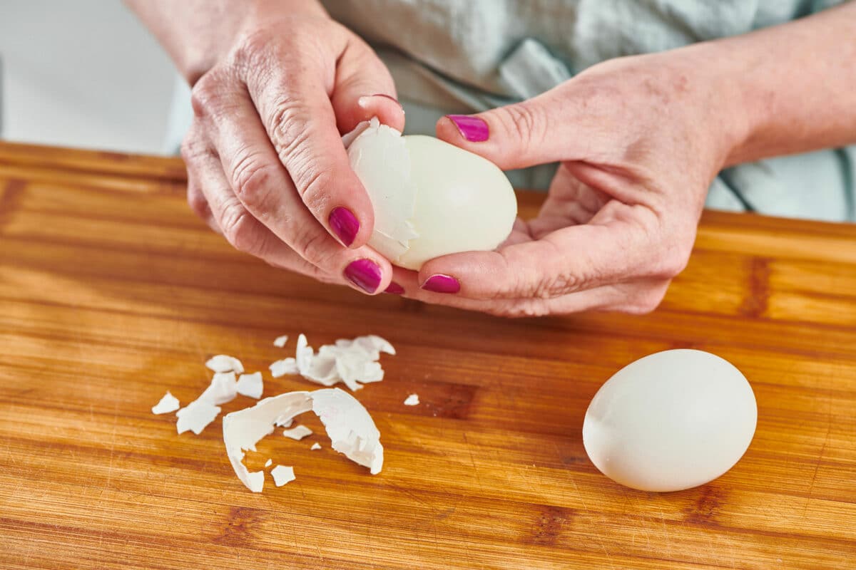 Woman peeling the shell off of a hard boiled egg.
