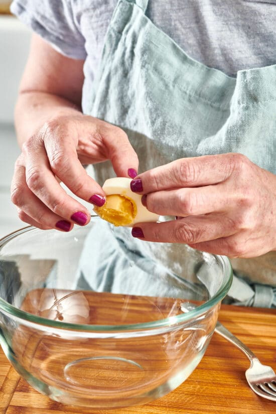 Woman removing the yolk from a hard boiled egg.