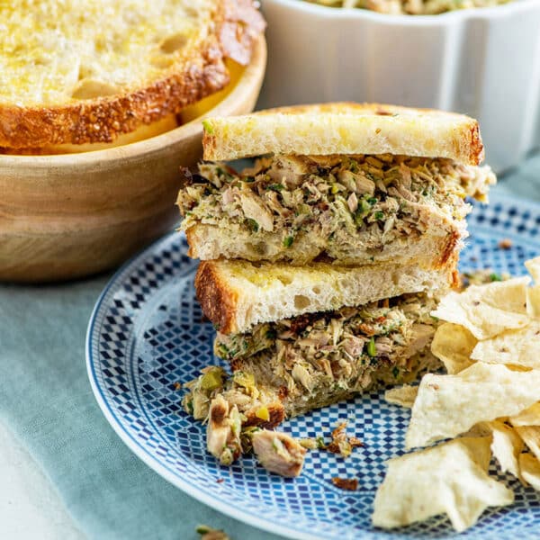 Slices of Italian tuna salad sandwiches stacked on blue plate with potato chips.