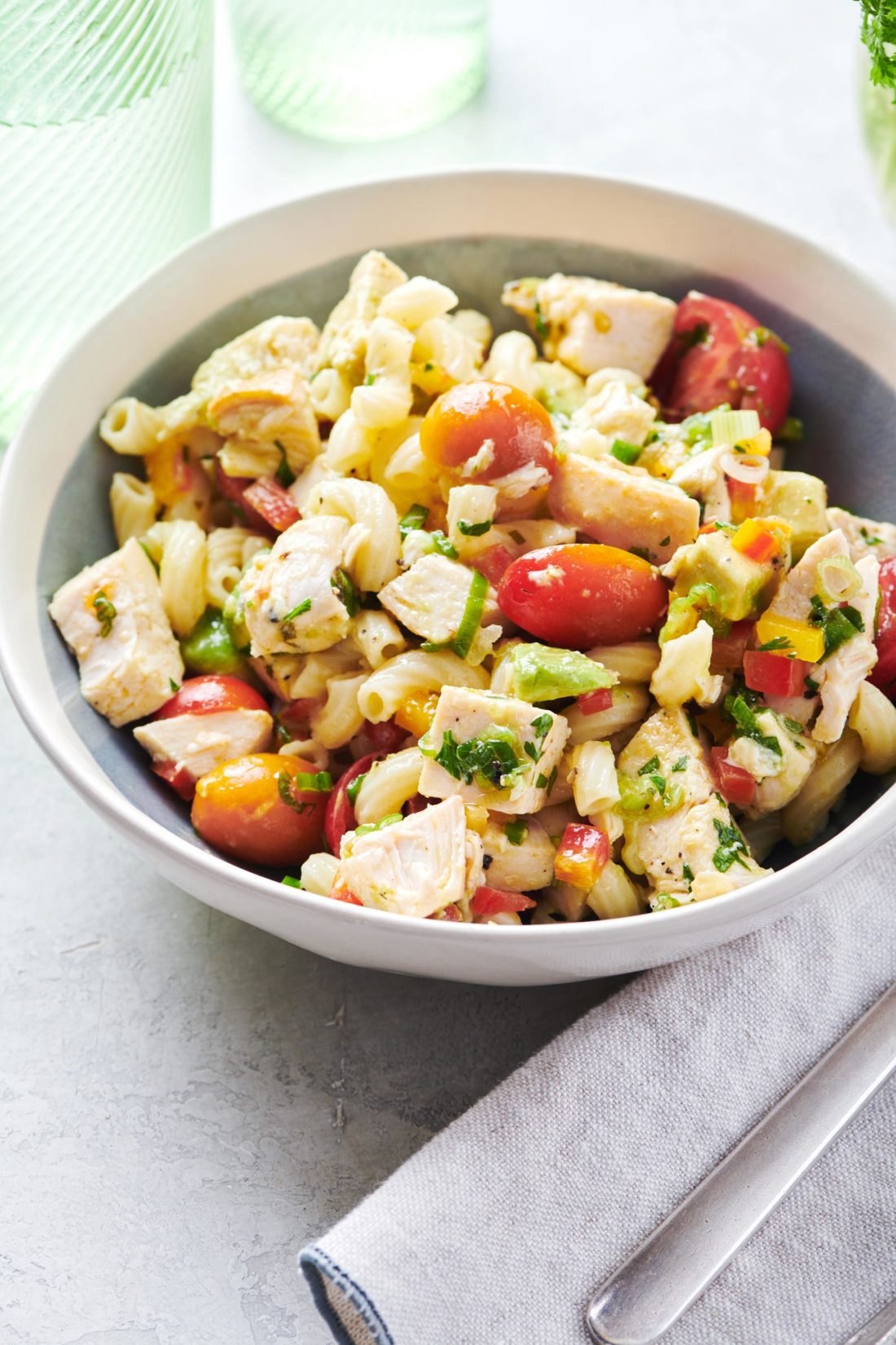 Bowl of Pasta Salad with Chicken, Avocado and Tomato on a table.