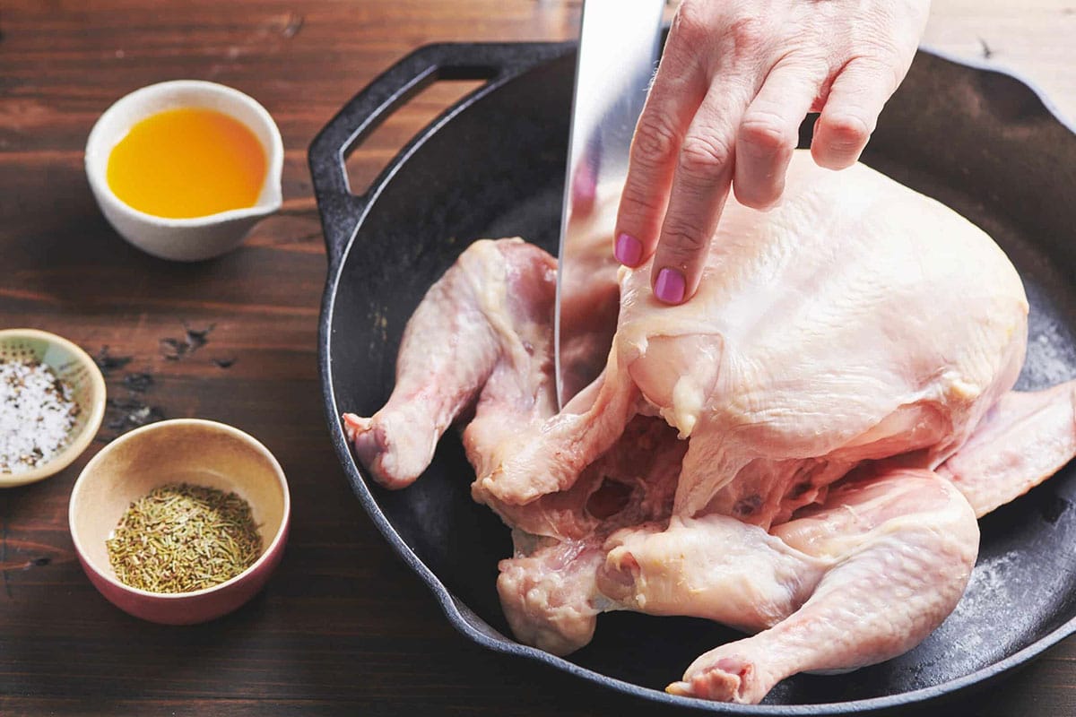 Woman cutting the thigh area of a raw chicken.