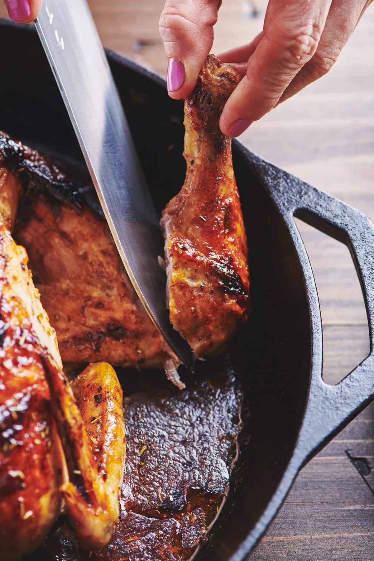 Woman carving glazed roast chicken with knife.