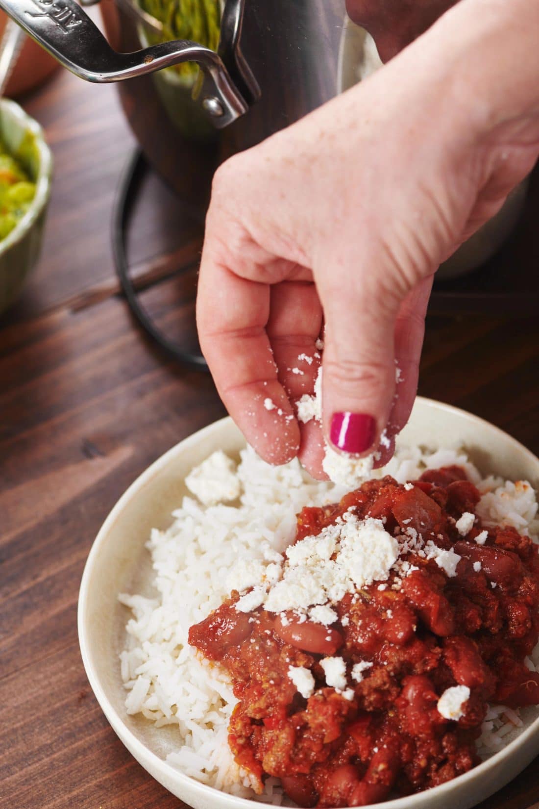 Woman sprinkling cheese onto a bowl of  Beef Chili and rice.