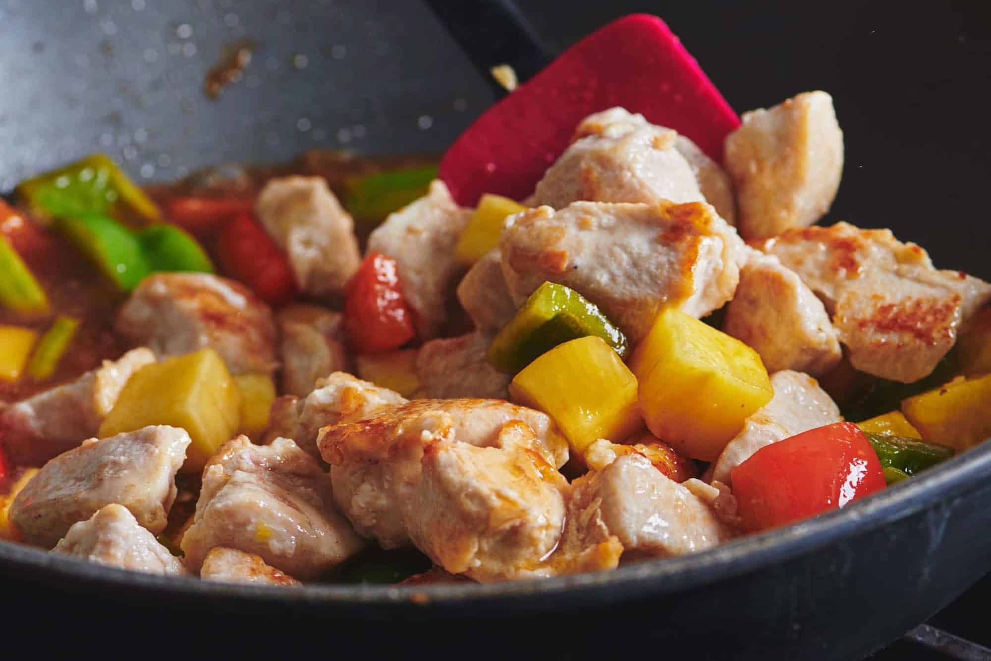 Spatula stirring Sweet and Sour Chicken with vegetables and pineapple chunks.