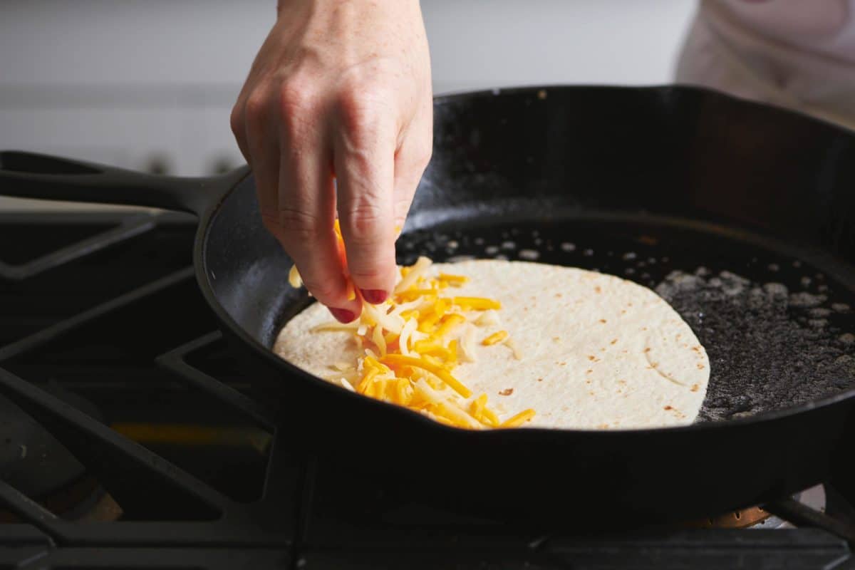 Woman sprinkling cheese onto a tortilla in a skillet.