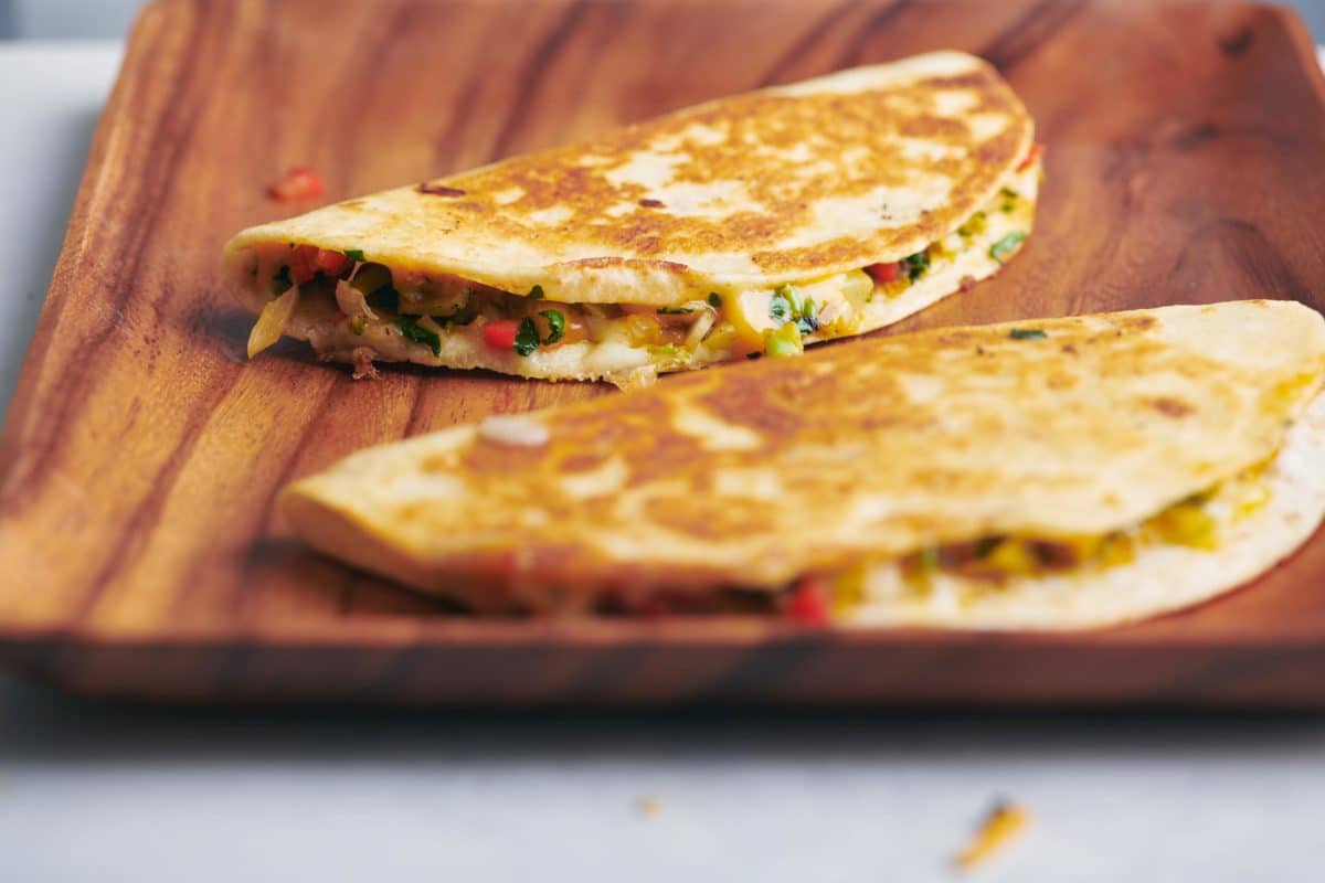 Two uncut Vegetable Quesadillas on a wooden plate.