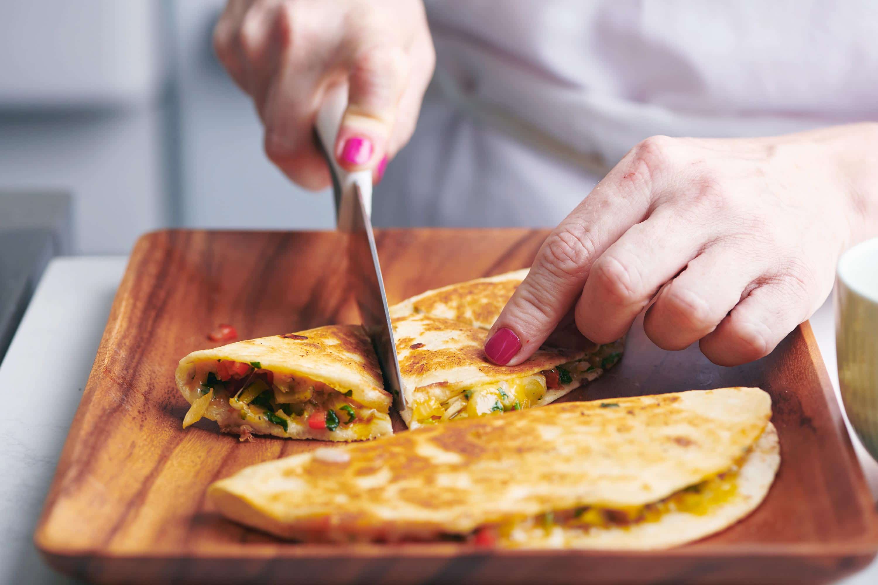 Woman slicing a Vegetable Quesadilla on a wooden board.