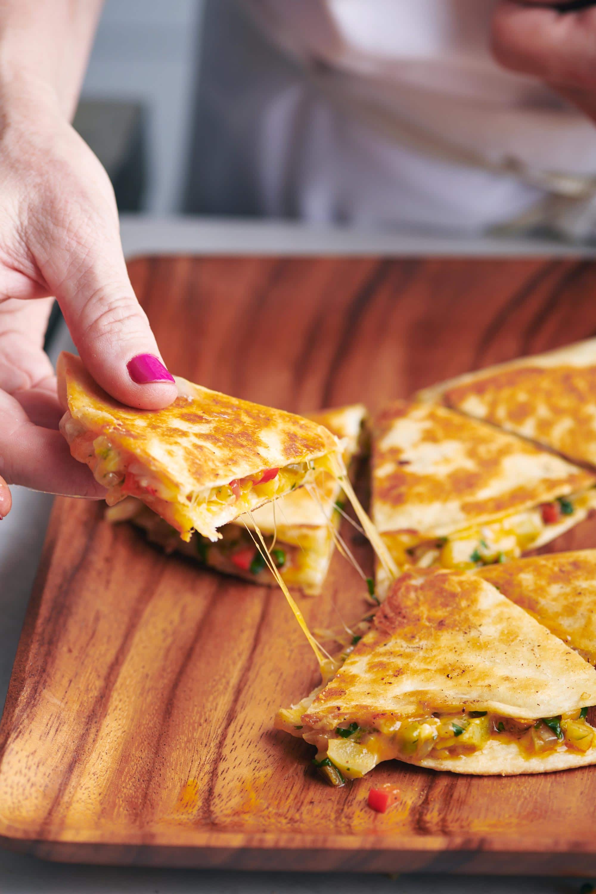 Woman grabbing a Vegetable Quesadilla from a wooden tray.
