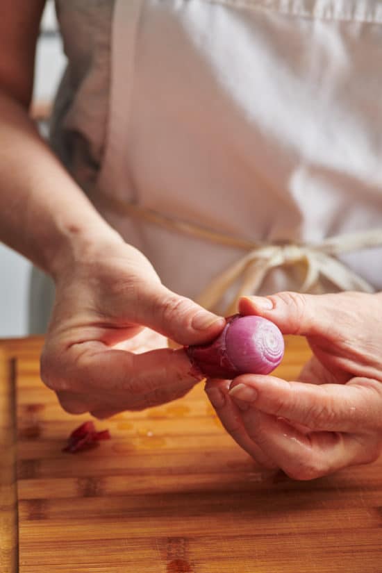 Woman sliding the peel off of a red pearl onion.