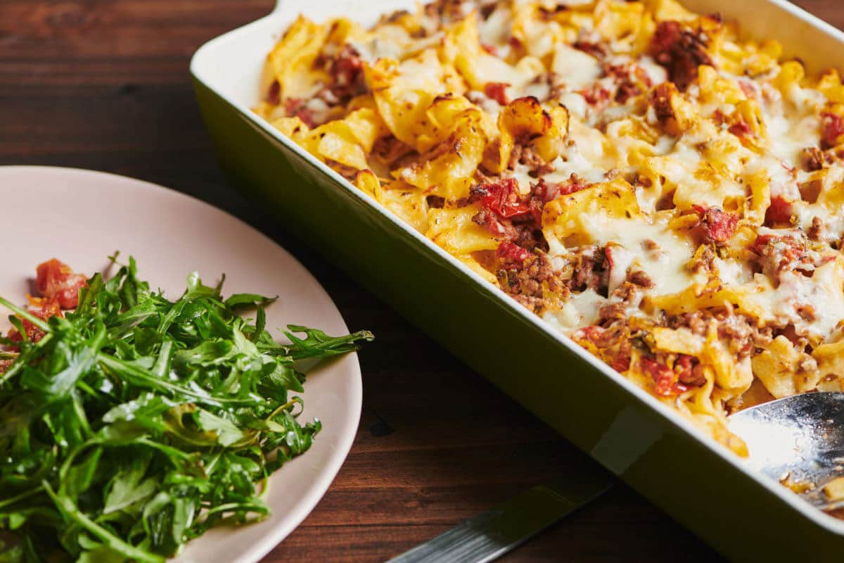 Beef and and cheese casserole in pan on table with plated salad.