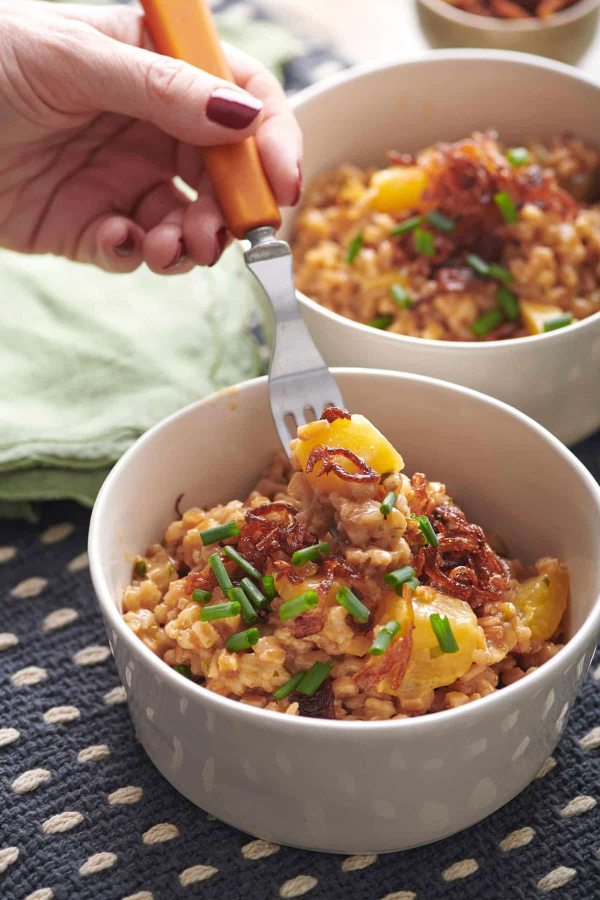 Fork scooping Farrotto with Golden Beets, Mixed Herbs and Crispy Shallots from a bowl.