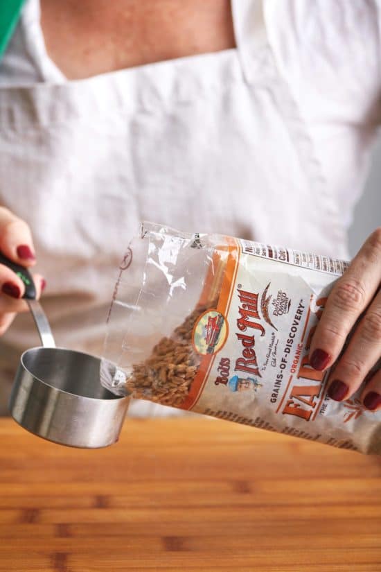 Woman pouring Bob\'s Red Mill Farro into a measuring cup.