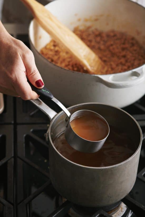 Woman holding a measuring cup of broth next to a Dutch Oven.