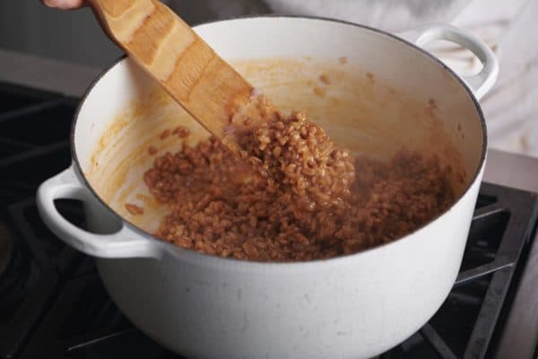 Wooden spatula stirring a white Dutch Oven of farro.