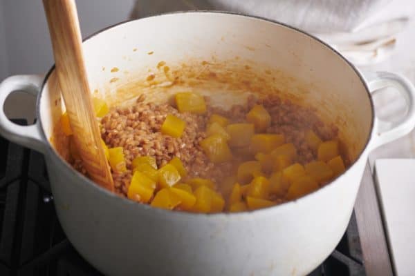 Wooden spatula stirring golden beets into a farro mixture in a Dutch oven.