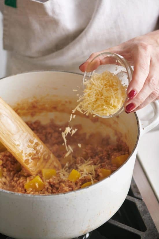Woman sprinkling parmesan into a Dutch Oven with farro and beets.