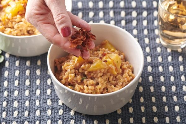 Woman topping a bowl of farrotto with crispy shallots.