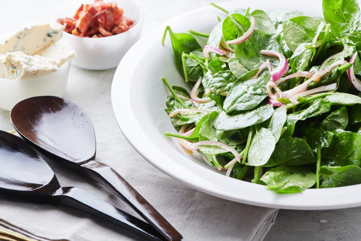 Bowl of Spinach Salad with bowls of Bacon and Blue Cheese on the side.