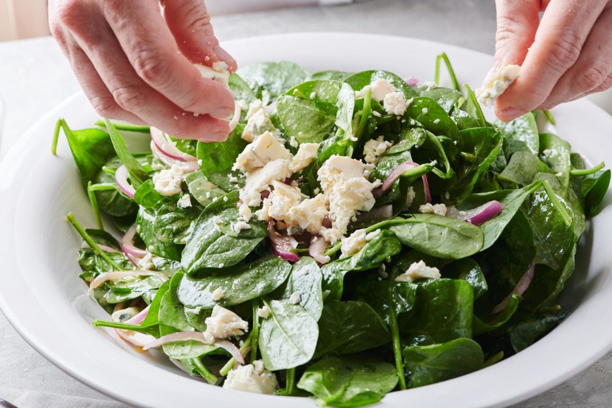 Woman crumbling blue cheese onto a Spinach Salad.
