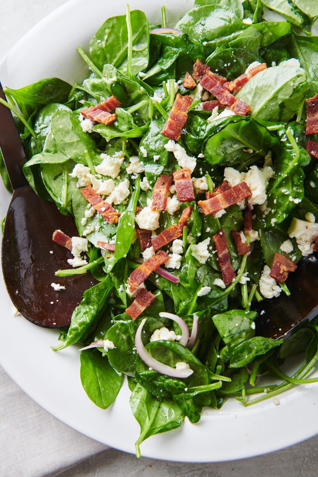 Spoon in a bowl of Spinach Salad with Bacon and Blue Cheese.