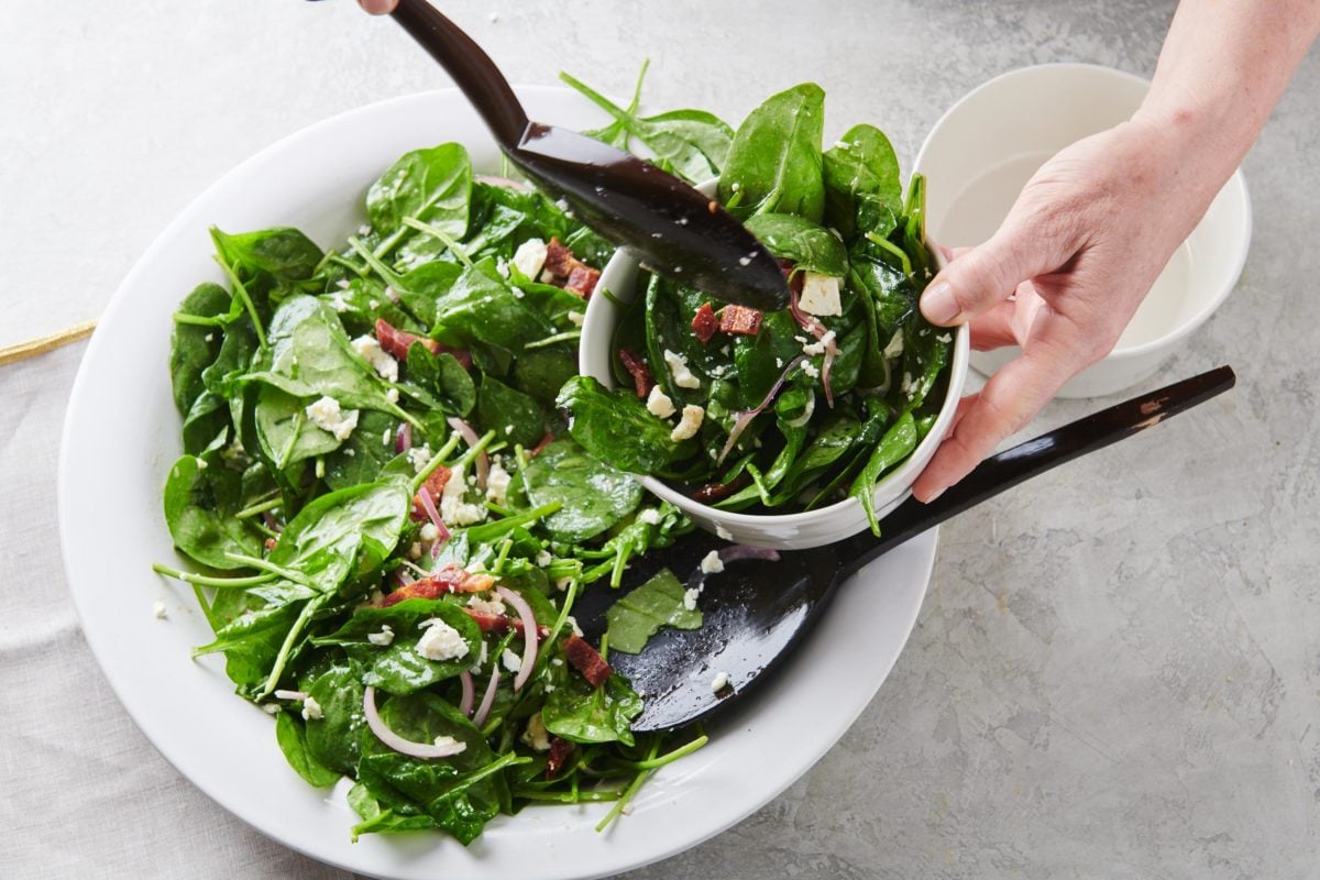 Spoon scooping Spinach Salad with Bacon and Blue Cheese into a bowl.