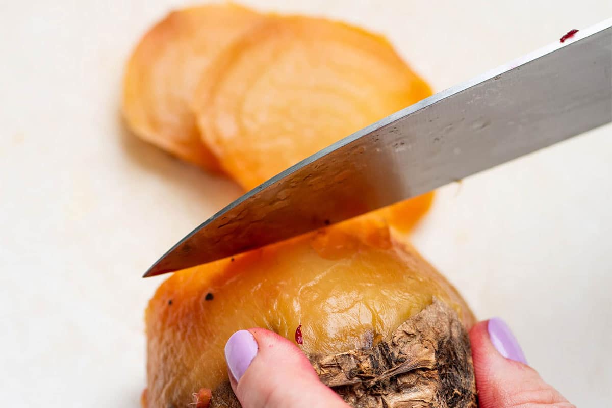 Woman slicing roasted golden beet with knife.