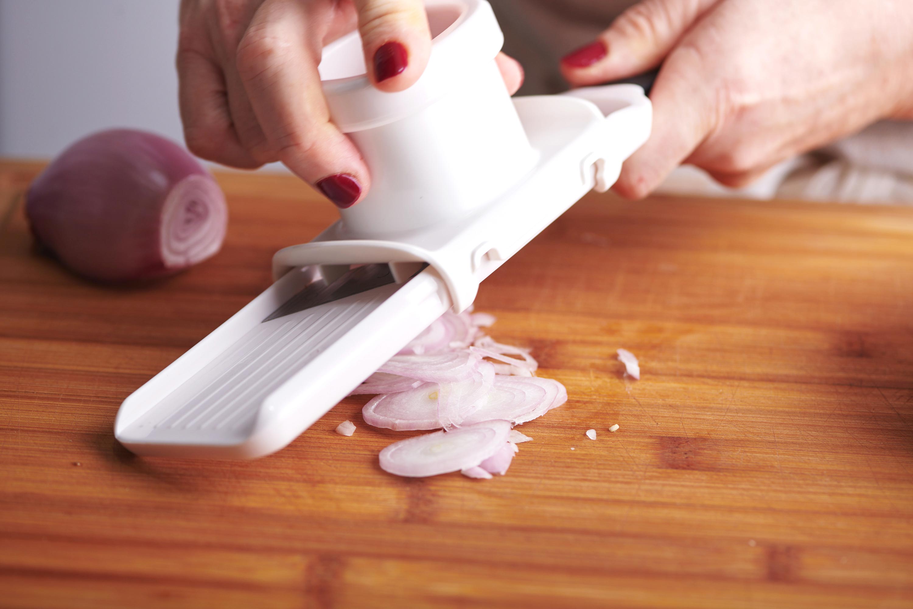 Woman slicing shallots with a vegetable slicer.