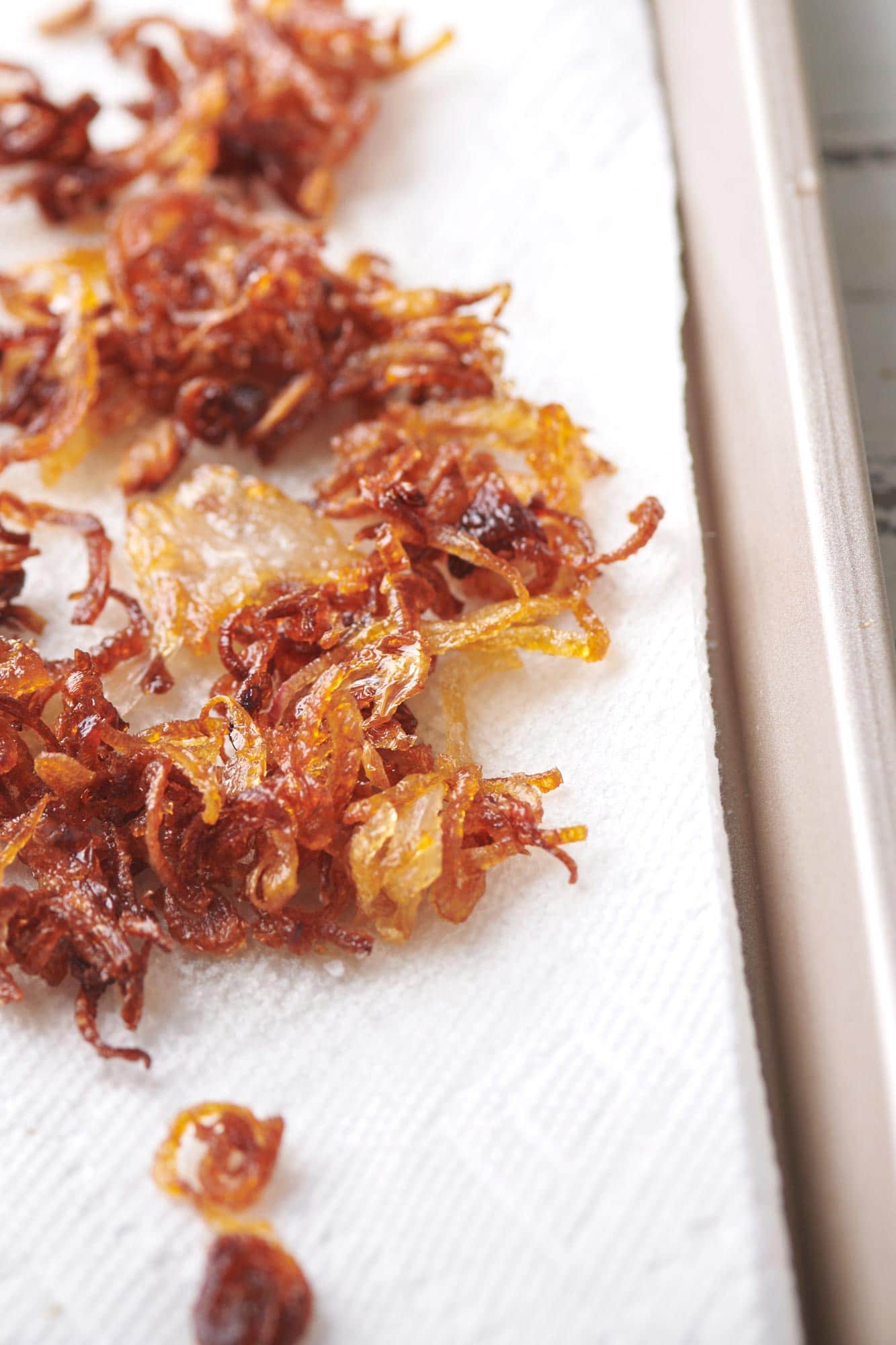 Pile of crispy shallots on paper towel-lined baking sheet.