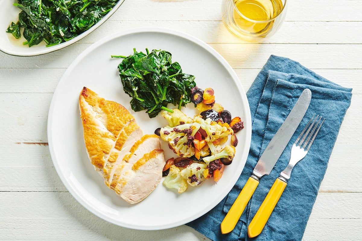 Chicken breast with roasted vegetables and sauteed spinach on a white plate.