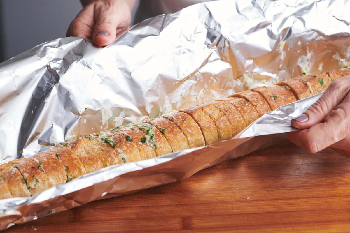 Woman wrapping a sliced and seasoned baguette in foil.