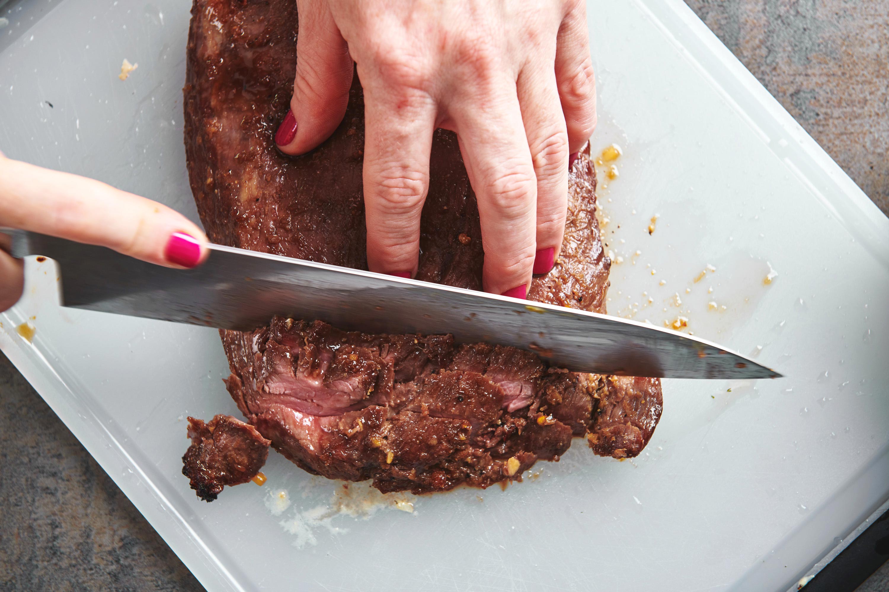 Woman slicing Soy-Ginger Flank Steak on a cutting board.