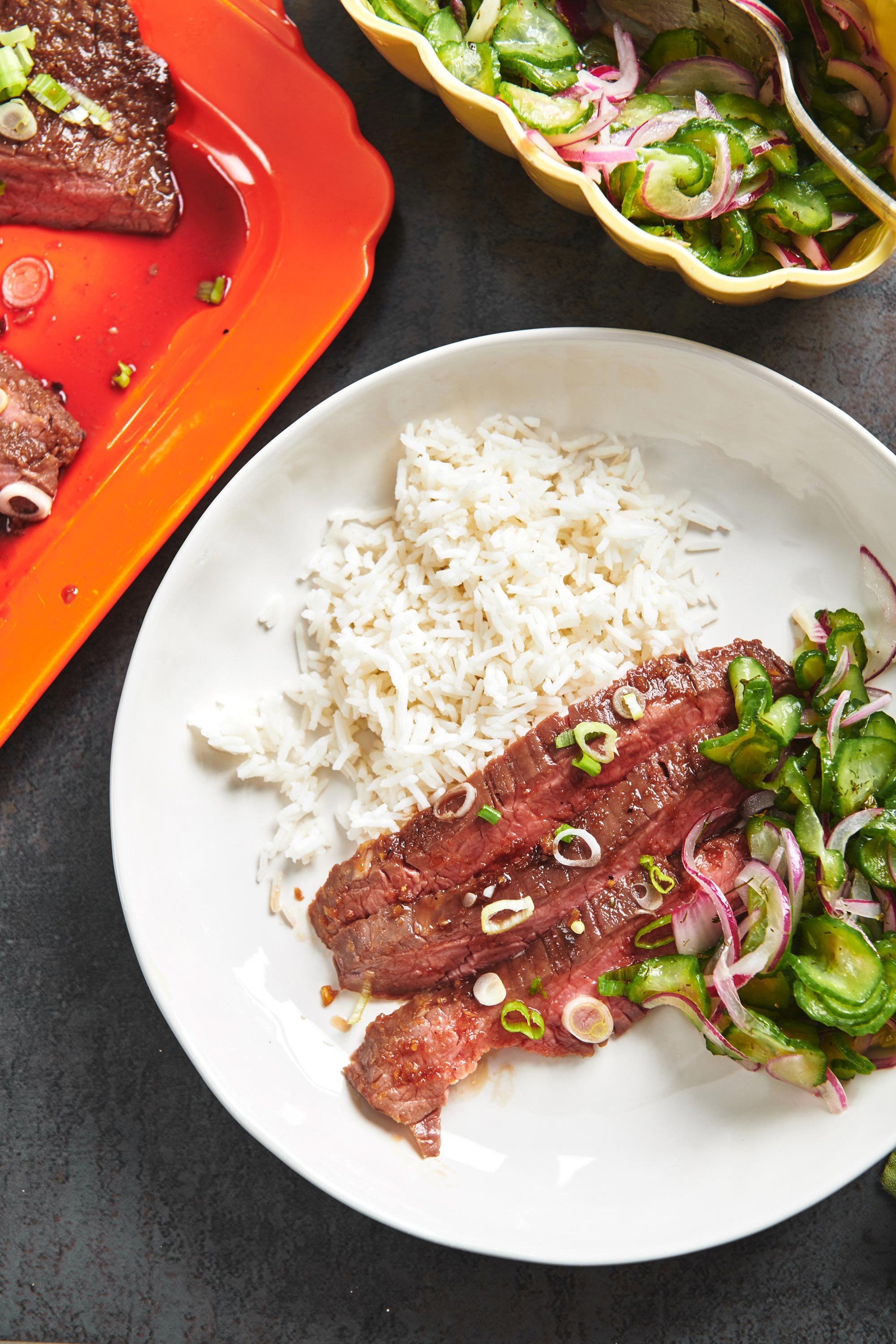 Slices of Soy-Ginger Flank Steak on a plate with rice and salad.