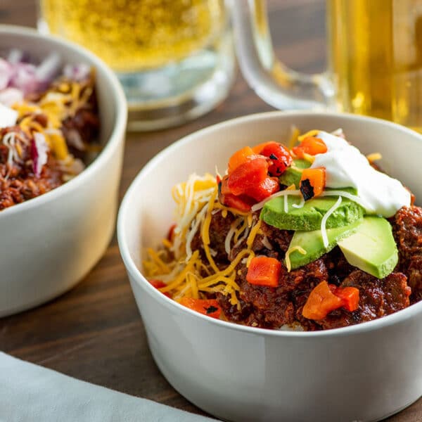 Texas chili in white bowls topped with avocado, cheese, tomatoes, and sour cream.