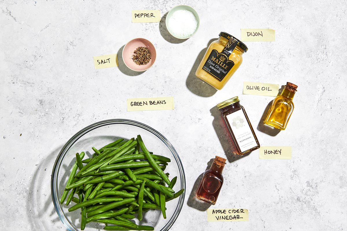 Fresh green beans, honey, mustard, and other ingredients on white marble.