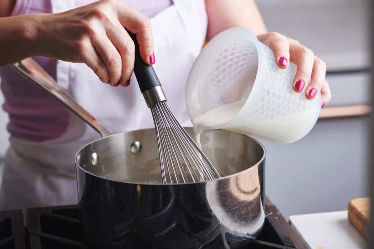 Woman whisking milk into a pan.