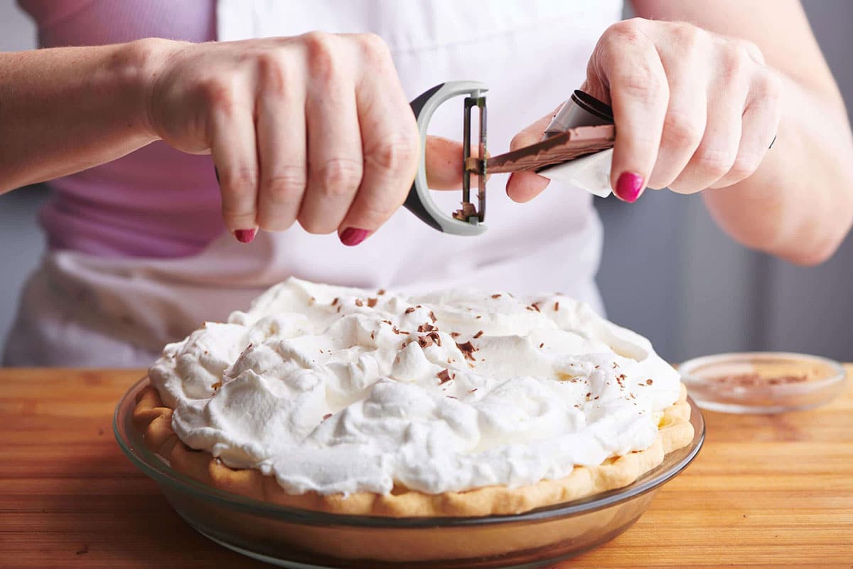Woman peeling chocolate onto a Banana Cream Pie.