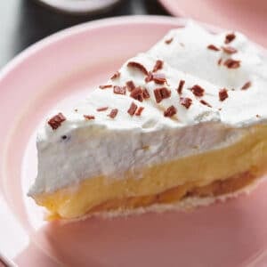 Slice of banana cream pie on pink plate.