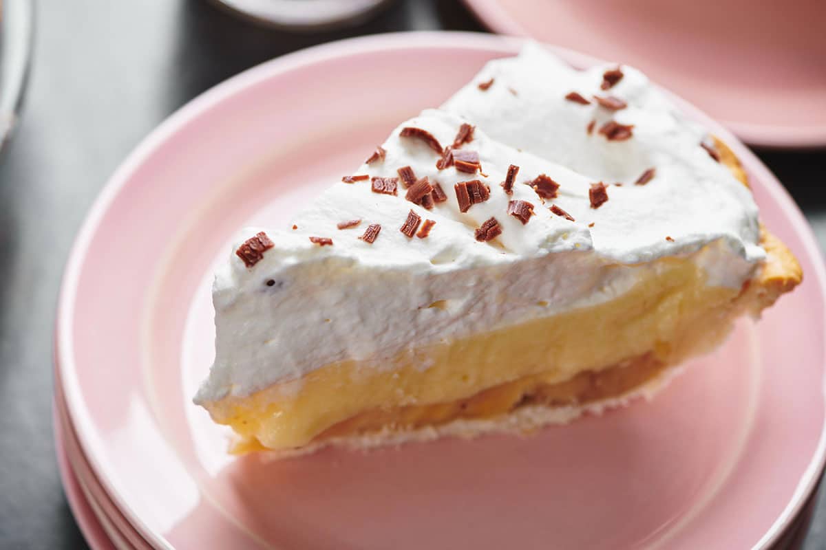 Slice of banana cream pie on pink plate.