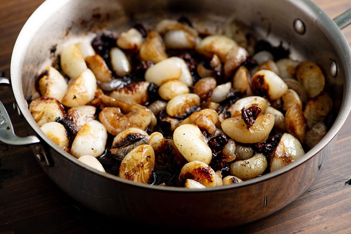 Braised Cipollini Onions with Dried Cherries in metal pan on table.